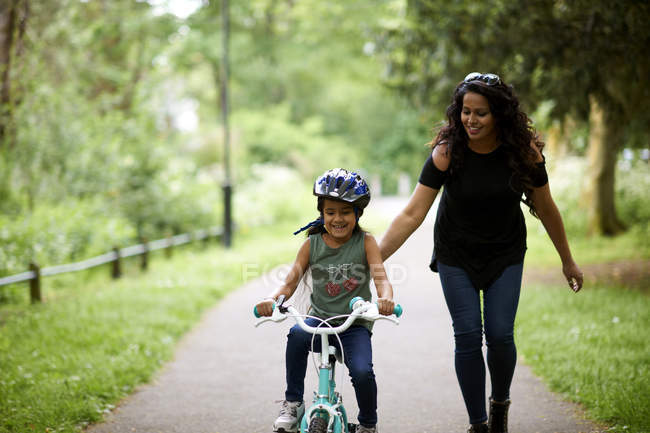 Madre feliz enseñando a su hija a montar en bicicleta - foto de stock