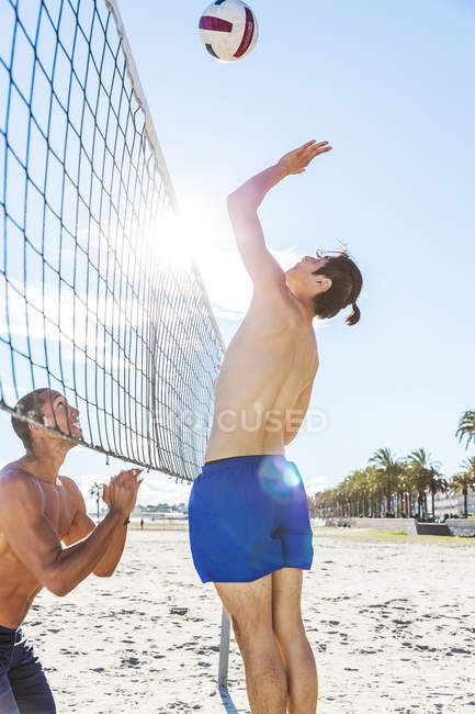 Hommes jouant au beach volley sur une plage ensoleillée — Photo de stock