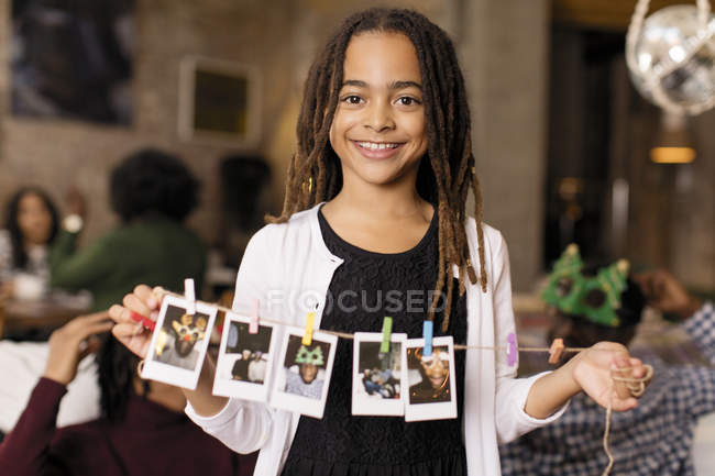 Portrait smiling girl holding string of instant photos — Stock Photo