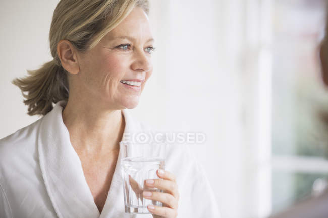 Усміхнена зріла жінка в халаті п'є воду — стокове фото
