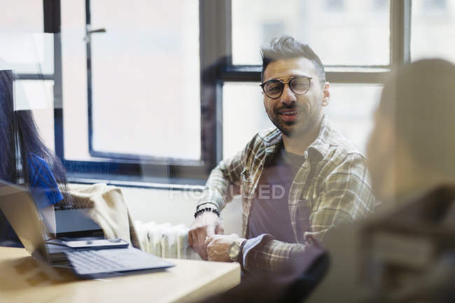 Uomo d'affari sorridente al computer portatile che parla con il collega in riunione di ufficio — Foto stock