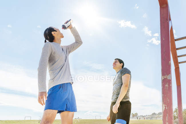Male runners resting, drinking water at sunny park — Stock Photo