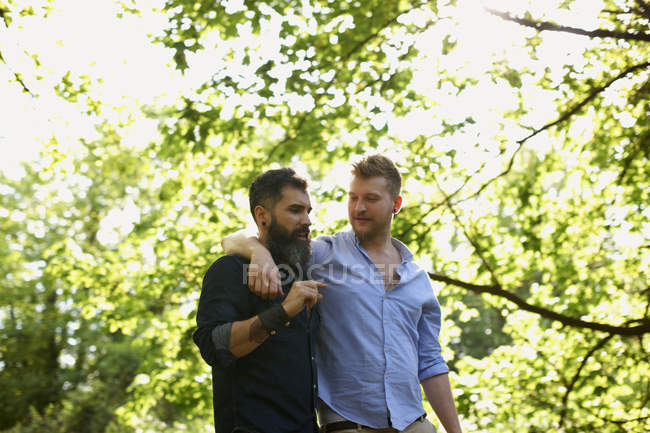 Ласковая гей-пара, гуляющая в солнечном парке — стоковое фото