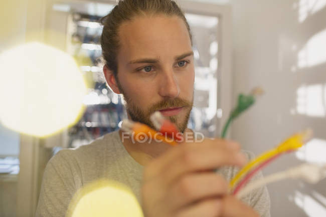 Curious IT technician examining multicolor connection plugs — Stock Photo