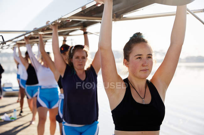Confident, determined female rowing team lifting scull overhead — Stock Photo