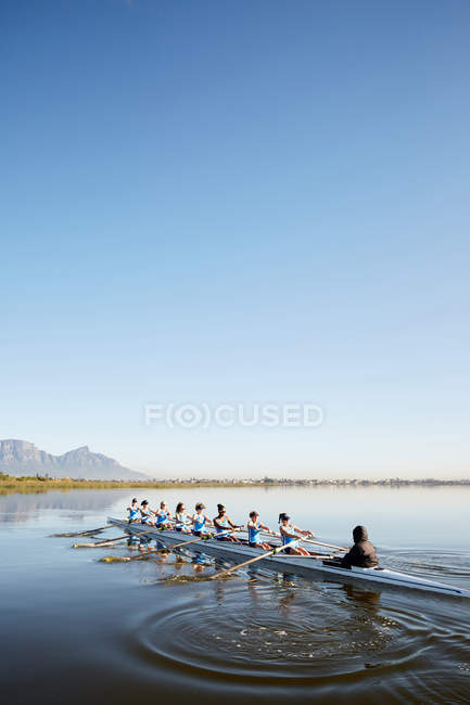 Remadores fêmea scull remo no lago tranquilo sob o céu azul — Fotografia de Stock