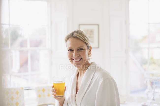 Portrait smiling, confident mature woman in bathrobe drinking juice — Stock Photo