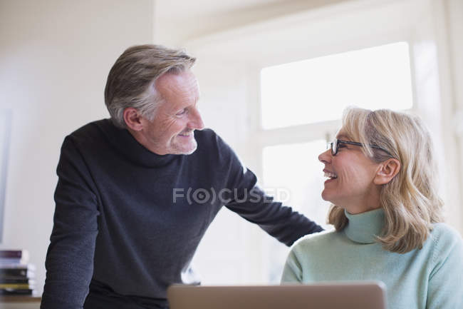 Sorridente coppia matura parlando al computer portatile a casa moderna — Foto stock