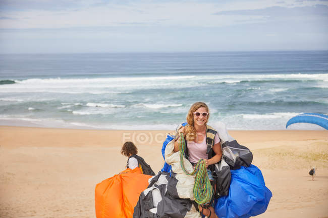 Portrait smiling, confident female paraglider with equipment on sunny ocean beach — Stock Photo