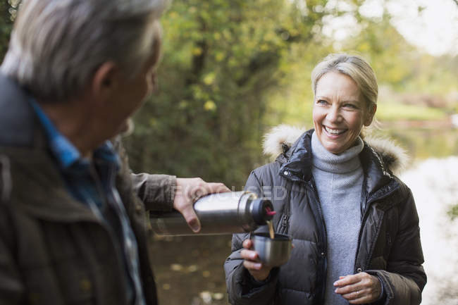 Mature caucasian couple drinking hot tea from thermos bottle in autumn park — Stock Photo