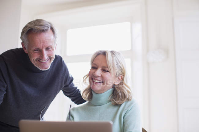 Sorrindo casal maduro usando laptop em casa moderna — Fotografia de Stock