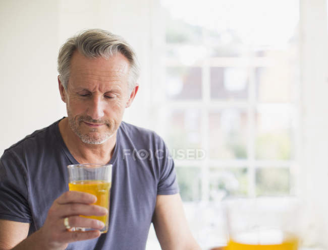Hombre maduro bebiendo jugo en casa moderna - foto de stock