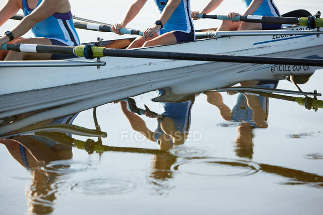 Reflection of female rowers rowing scull on lake — Stock Photo