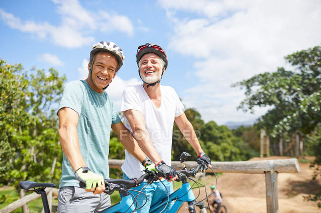 Portrait confident father and son mountain biking on sunny trail — Stock Photo
