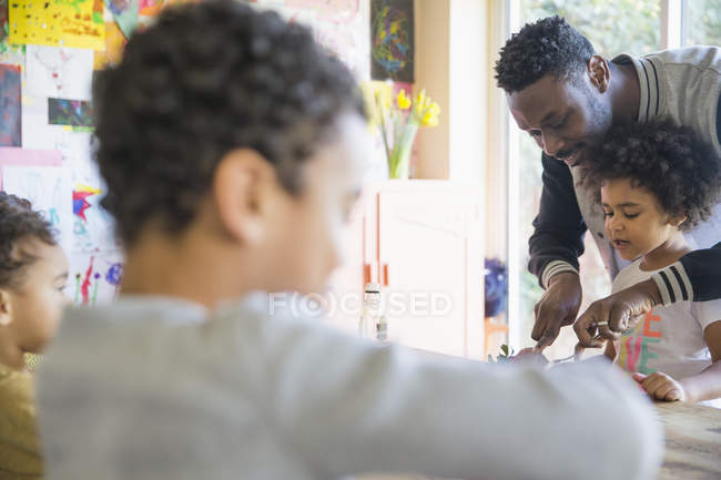 Father helping cut food for daughter at table — Stock Photo