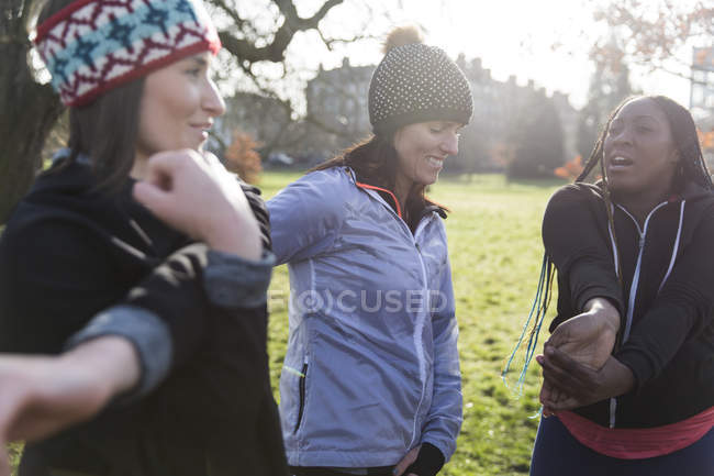 Corredores femininos se alongando no parque ensolarado — Fotografia de Stock