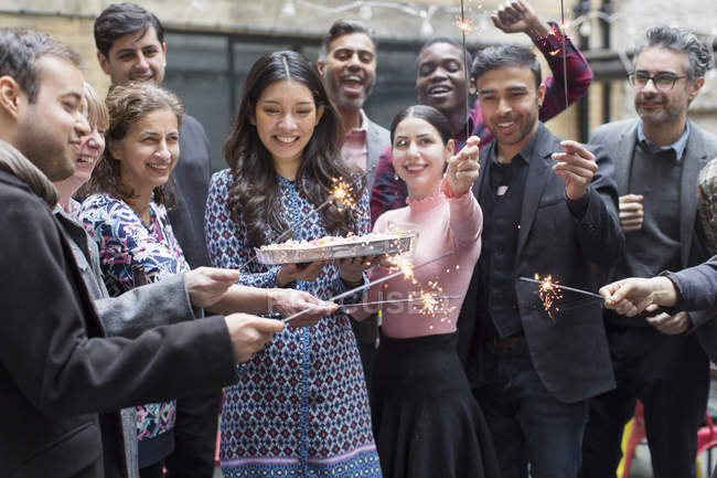 Друзі з блискітками святкують з жінкою, яка тримає торт на день народження — стокове фото
