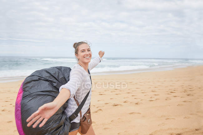 Портрет улыбающейся, беззаботной молодой парапланеристки с парашютным рюкзаком на берегу океана — стоковое фото