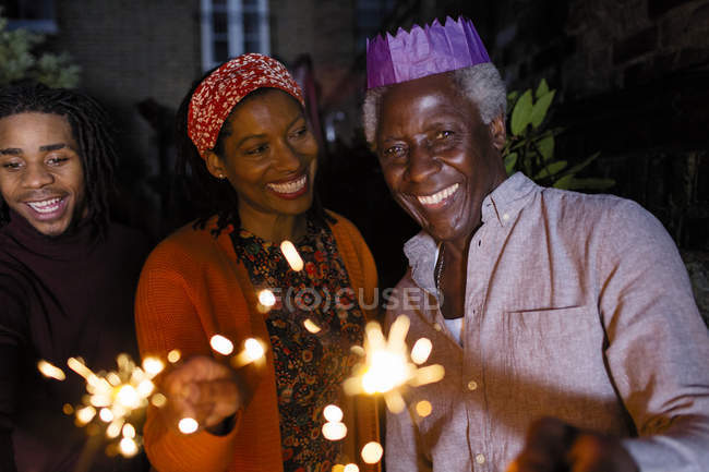 Portrait smiling senior father with sparklers in paper crown celebrating with daughter — Stock Photo