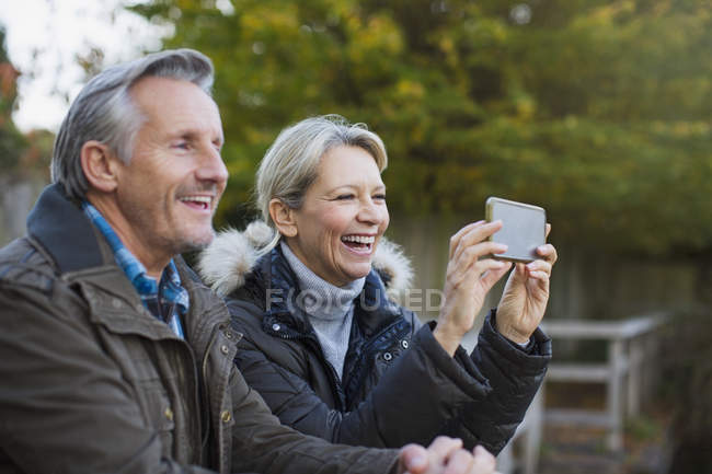 Зріла біла пара фотографується на смартфоні в осінньому парку — стокове фото