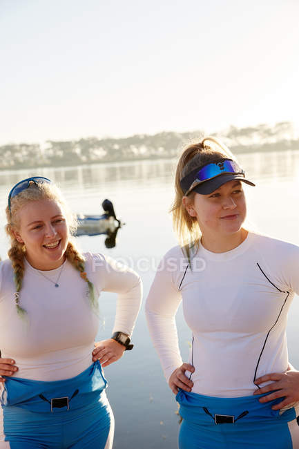 Female rowers with hands on hips at sunny lakeside — Stock Photo