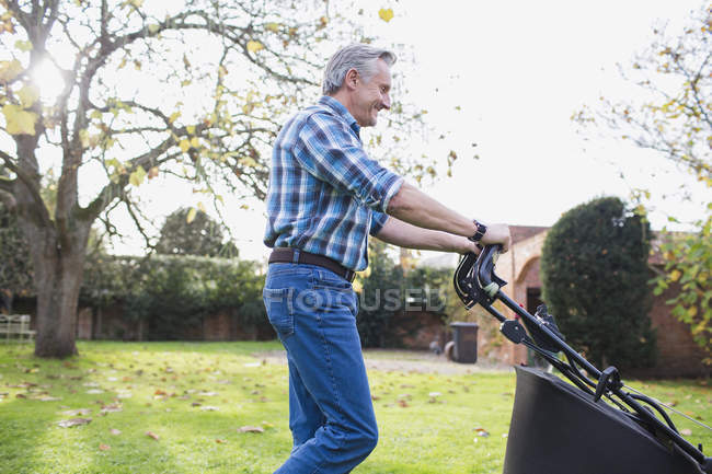 Vista lateral do homem caucasiano maduro com cortador de grama trabalhando no jardim — Fotografia de Stock