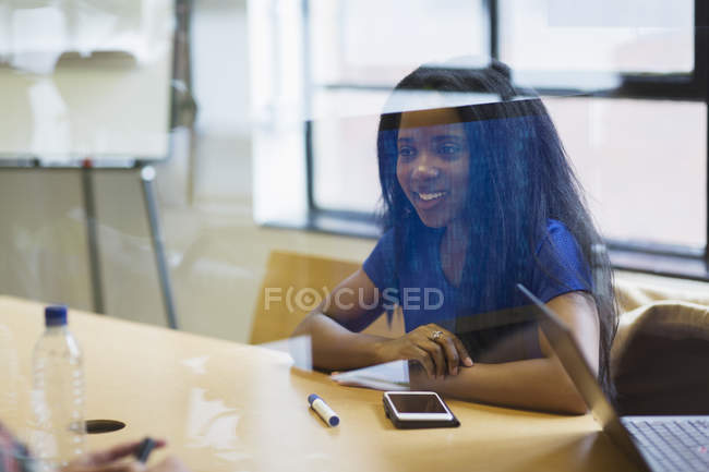 Smiling young businesswoman with smart phone listening in meeting — Stock Photo