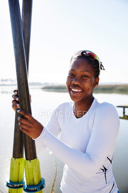 Ritratto sorridente, fiducioso vogatore femminile che regge remi sul lungolago soleggiato — Foto stock