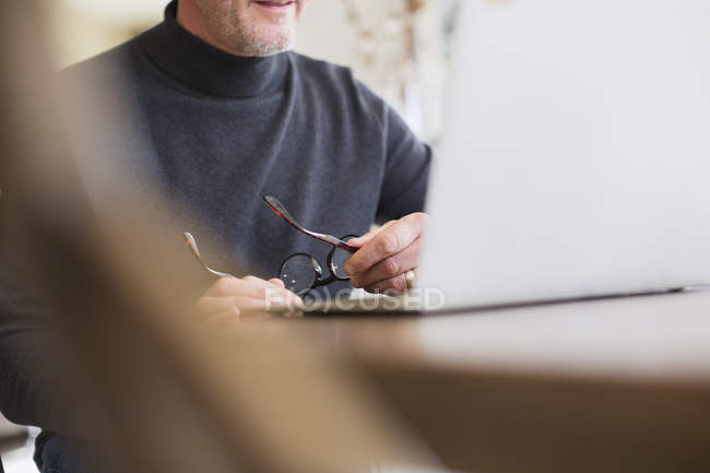 Maturo freelance di sesso maschile che tiene gli occhiali, lavorando al computer portatile — Foto stock