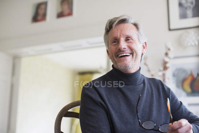 Laughing mature man holding eyeglasses at modern home — Stock Photo