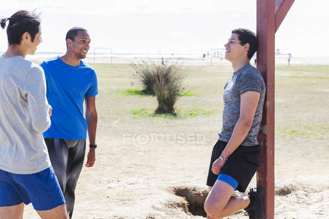 Male runners resting, talking in sunny park — Stock Photo