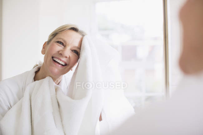 Lächeln reife Frau trocknet Gesicht mit Handtuch am Badezimmerspiegel — Stockfoto