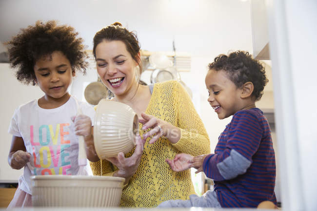Madre e hijos felices horneando en la cocina - foto de stock