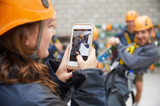 Femme avec appareil photo téléphone photographier des amis dans l'équipement de tyrolienne — Photo de stock