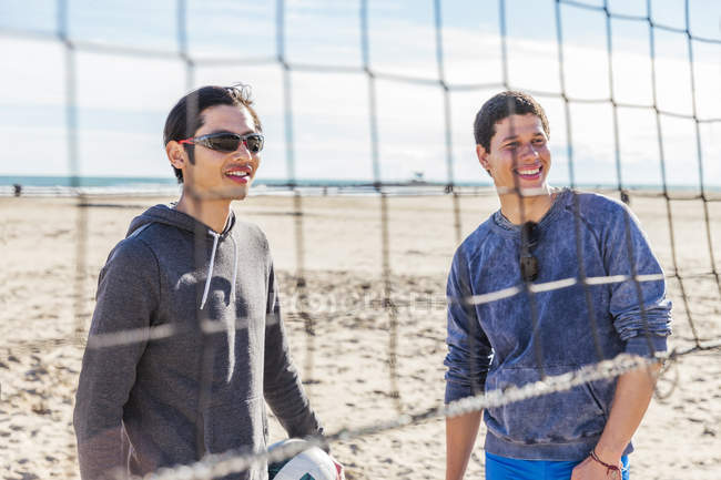 Sorrindo homens jogando vôlei de praia na praia ensolarada — Fotografia de Stock