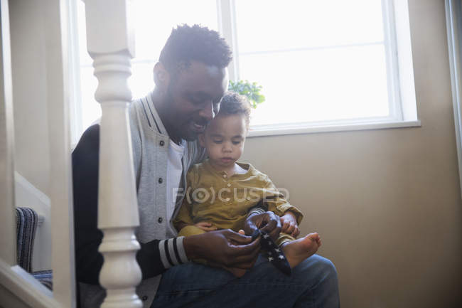 Padre poniendo zapatos en bebé hijo en escaleras - foto de stock