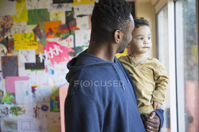 Afroamericano padre mirando por la ventana con hijo - foto de stock