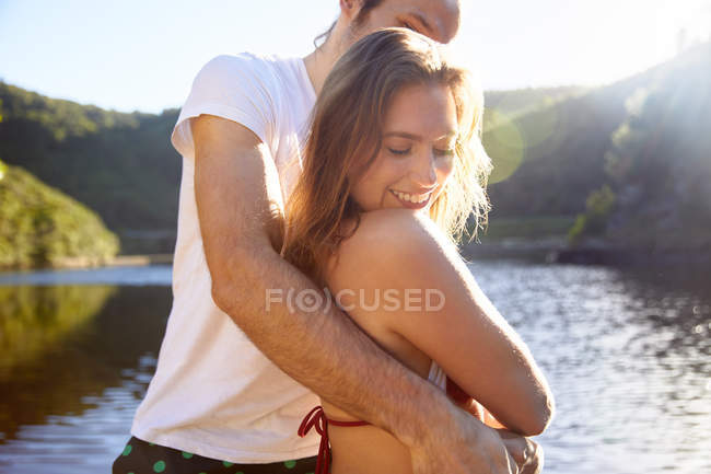 Cariñosa pareja abrazándose en el soleado lago de verano - foto de stock
