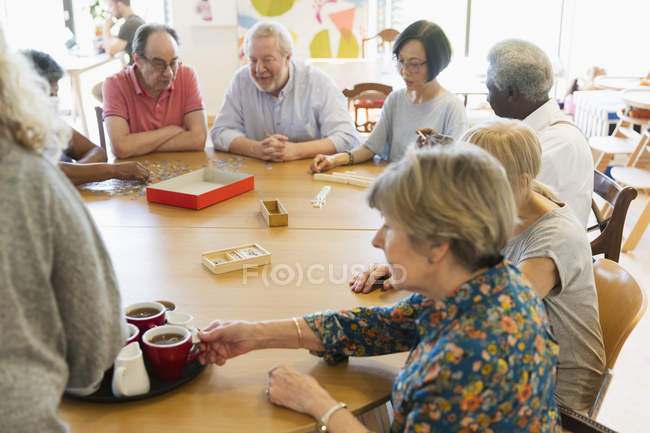 Senior friends playing games and drinking tea at table in community center — Stock Photo