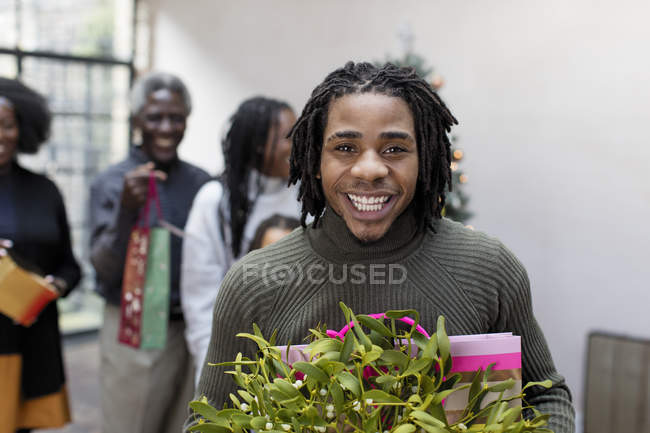 Portrait smiling, enthusiastic young man with Christmas gift and mistletoe — Stock Photo