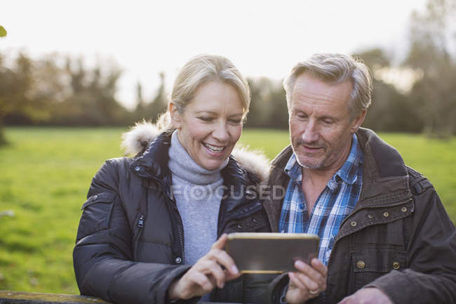 Зріла біла пара використовує смартфон в осінньому парку — стокове фото