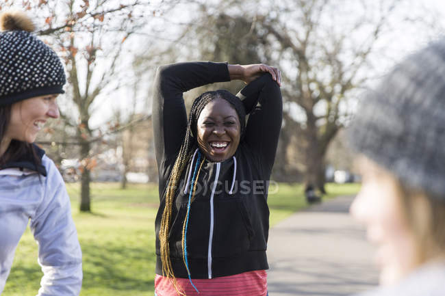 Sorridente corridore femminile che si estende nel parco soleggiato — Foto stock