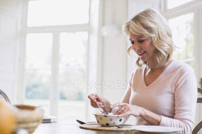 Sorridente donna matura che fa colazione a casa moderna — Foto stock