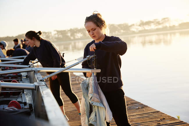 Female rowers preparing scull on sunny lakeside dock — Stock Photo