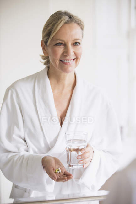 Smiling Mature Woman In Bathrobe Taking Vitamins At Bathroom Mirror — White Indoors Stock
