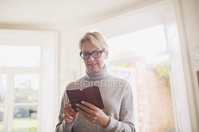 Donna matura che utilizza lo smartphone a casa moderna — Foto stock