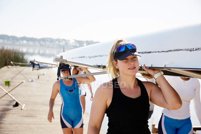 Female rowers carrying scull on sunny dock — Stock Photo