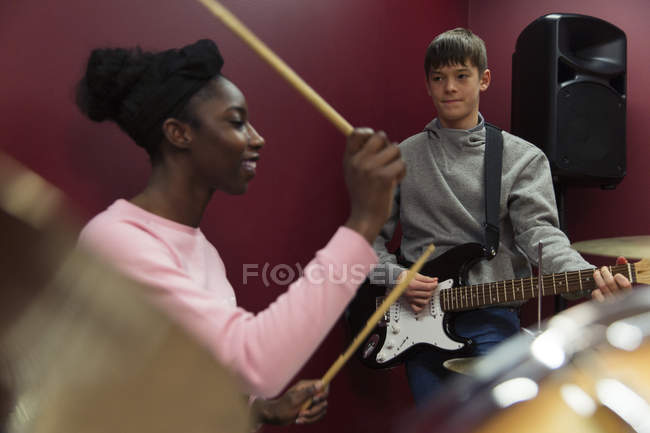 Підліткові музиканти записують музику, грають на гітарі та барабанах у звуковій кабіні — стокове фото