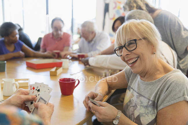 Feliz mujer mayor jugando a las cartas con un amigo en la mesa en el centro comunitario - foto de stock