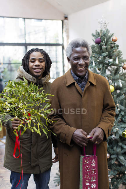 Portrait smiling grandfather and grandson arriving with Christmas gift and mistletoe — Stock Photo